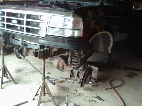 1996 Ford Bronco - Front end of a black truck, possibly a Ford F-Series from the early 1990s, undergoing maintenance with the front suspension disassembled.