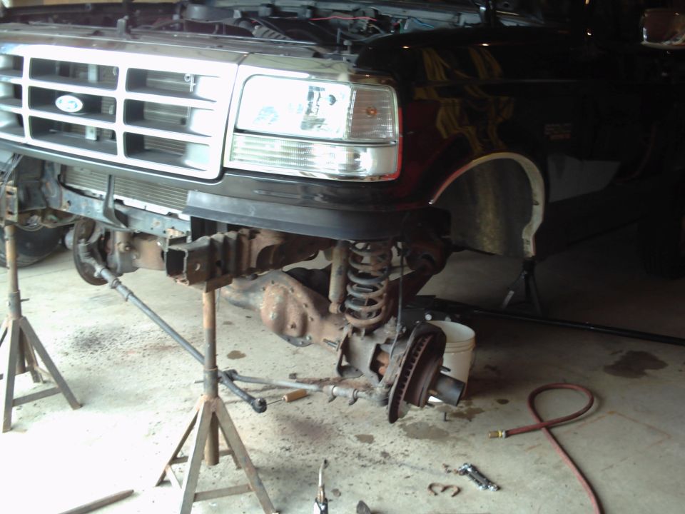 Front end of black truck on jack stands, showing grille and suspension components