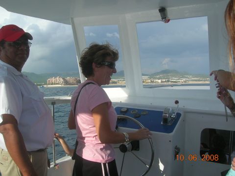 1985 Ford Bronco - A woman steers a boat with a man standing nearby, overlooking a coastal town.