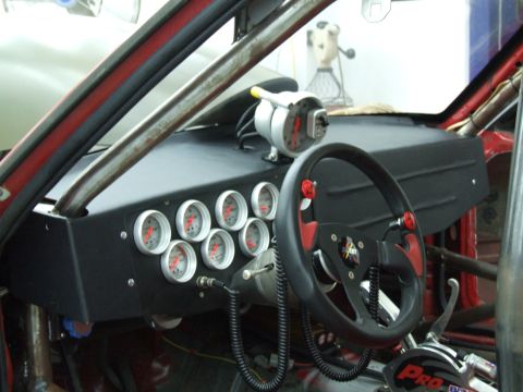 1990 Ford Mustang - The interior of a racing car shows a dashboard filled with gauges and a custom steering wheel.
