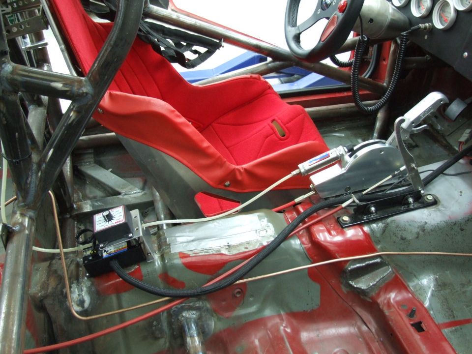 Racing car interior showing red bucket seat, roll cage, shifter, and gauges. SuperMotors logo visible