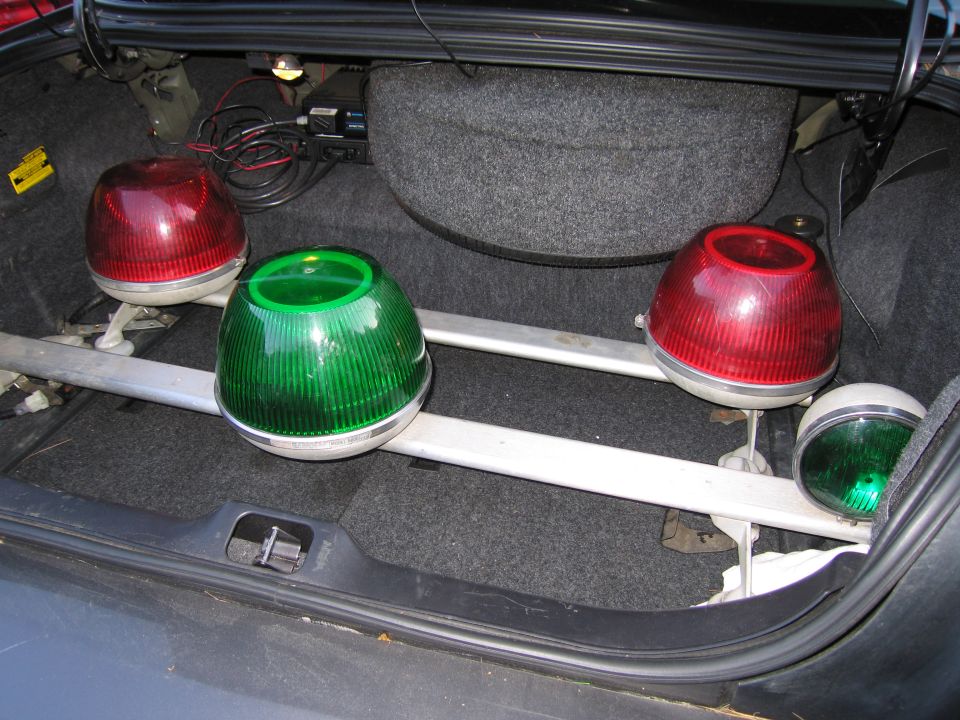 Car trunk with red and green emergency lights mounted on a bar. Spare tire and wiring are visible