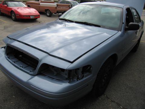 2001 Ford Crown Victoria - Front view of a light blue 2001 Ford Crown Victoria missing its grille and headlights. Other vehicles are parked behind it.