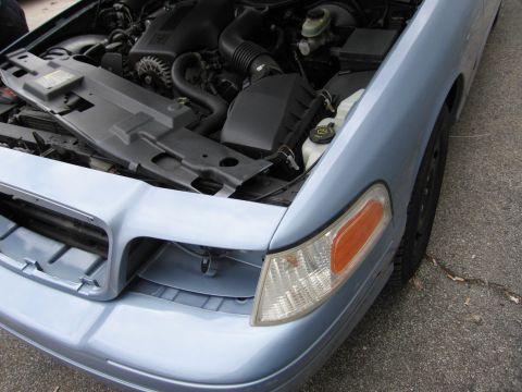 2001 Ford Crown Victoria - The engine bay of a light blue 2001 Ford Crown Victoria is visible with the hood open, revealing the engine and front fender.