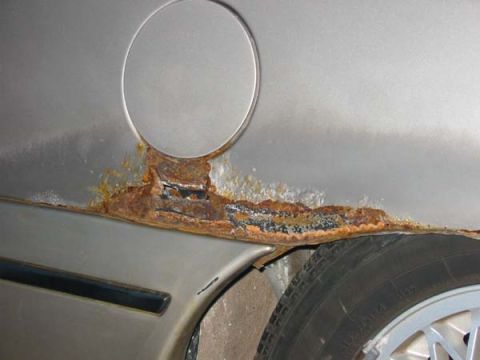 1990 Ford Taurus - Extensive rust damage is visible on the side panel of a silver vehicle, obscuring any specific model year details.