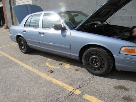 2001 Ford Crown Victoria - A light blue 2001 Ford Crown Victoria is parked with its hood and trunk open, revealing the engine bay and rear storage.