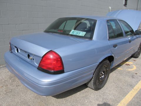 2001 Ford Crown Victoria - A light blue sedan is parked outside a brick building with its hood open. The license plate reads 82765.