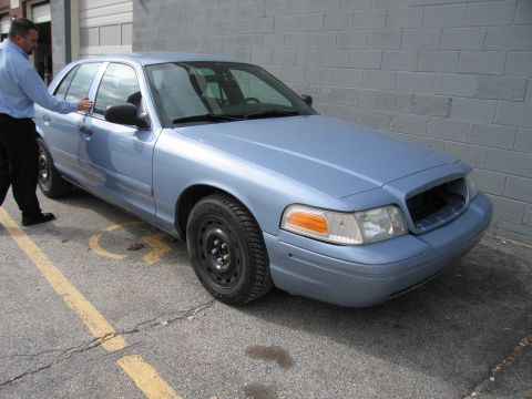 2001 Ford Crown Victoria - A light blue 2001 Ford Crown Victoria is parked in a handicapped spot next to a brick wall.