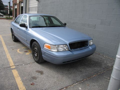 2001 Ford Crown Victoria - A blue 2001 Ford Crown Victoria is parked in front of a grey brick wall.