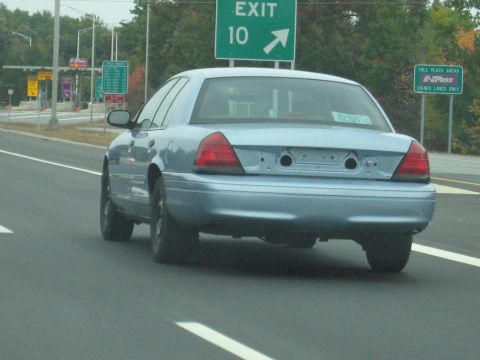 2001 Ford Crown Victoria - Rear view of a blue 2001 Ford Crown Victoria on the highway, approaching an exit and toll plaza.