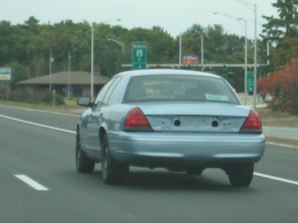 Light blue sedan driving on highway, rear view. Missing license plate and tow hitch