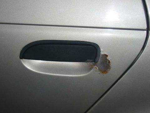 1990 Ford Taurus - Rust is forming on the exterior of a car door near the handle.