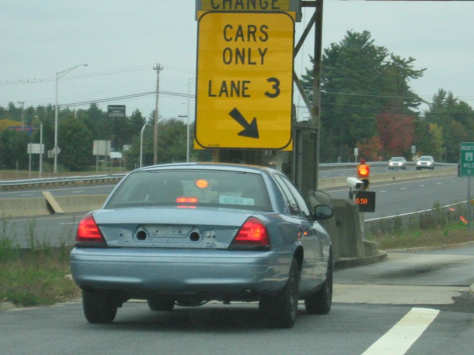 Light blue 2001 Ford Crown Victoria at a toll booth, rear view. Other cars visible on highway