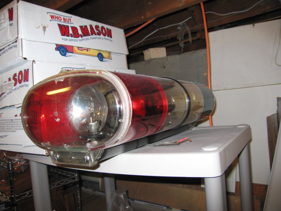 Red and clear emergency light bar with visible bulb, resting on a white table