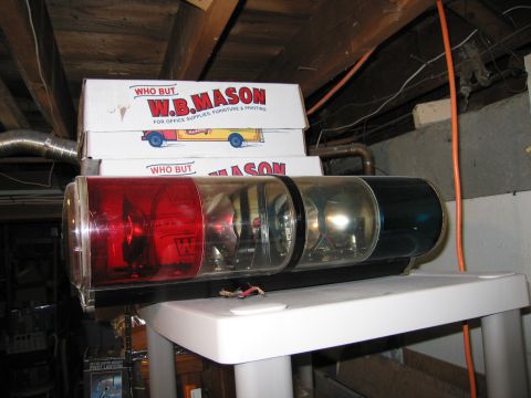 2001 Ford Crown Victoria - Emergency light bar with red and blue lenses sits atop stacked W.B. Mason boxes in a cluttered storage area.