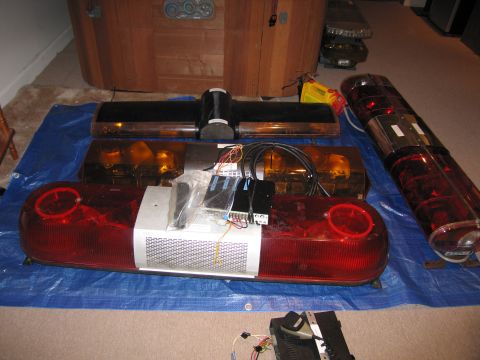 2001 Ford Crown Victoria - Collection of emergency light bars, some with wiring, displayed on a blue tarp indoors.