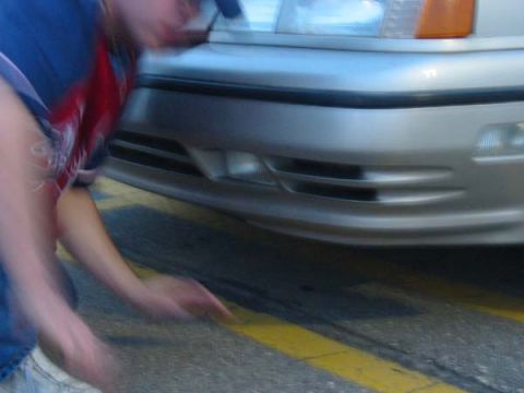 1990 Ford Taurus - Close-up of a car's front end with a person interacting with it near the bumper.