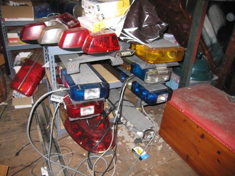 2001 Ford Crown Victoria - A collection of various emergency vehicle light bars and tail lights are stored in a cluttered space.