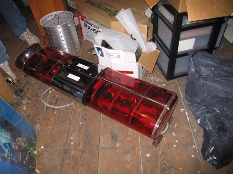 2001 Ford Crown Victoria - A red emergency light bar with chrome accents lies on a wooden floor amidst various stored items.