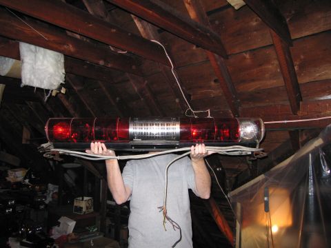 2001 Ford Crown Victoria - An emergency light bar is held up by a person in a cluttered attic space.