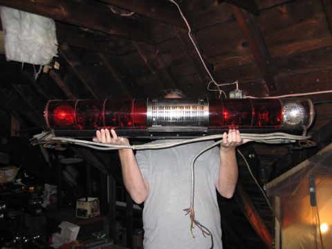 2001 Ford Crown Victoria - A person holds a red light bar with a chrome grille and exposed wires in an attic space.