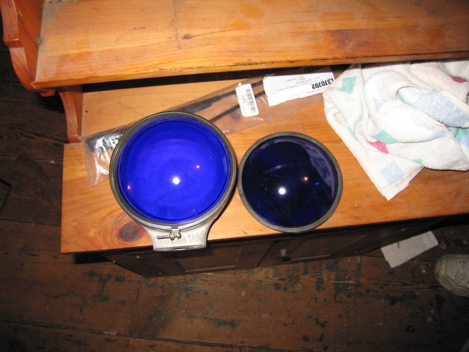 Two blue glass lenses, one larger than the other, sit on a wooden surface next to a folded towel and some packaging
