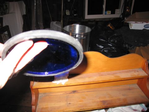 2001 Ford Crown Victoria - A hand holds a blue glass filter in front of a wooden shelf with various items in the background.