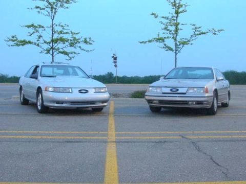 1990 Ford Taurus - Two 1990 Ford Taurus sedans are parked in a lot under a clear sky.