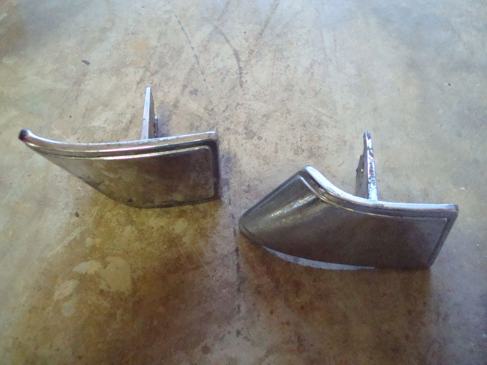 Two chrome door handles with mounting posts on a concrete surface