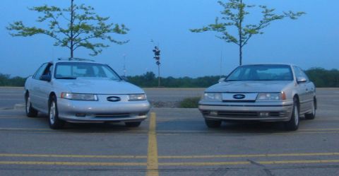 1990 Ford Taurus - Two Ford Taurus sedans are parked in a lot under a twilight sky.