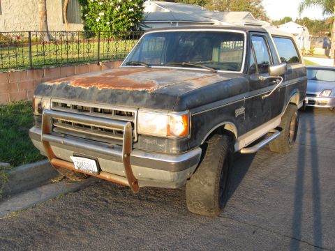 1990 Ford Bronco - This 1990 Ford Bronco features a prominent aftermarket bumper and a heavily rusted hood, indicating significant wear.