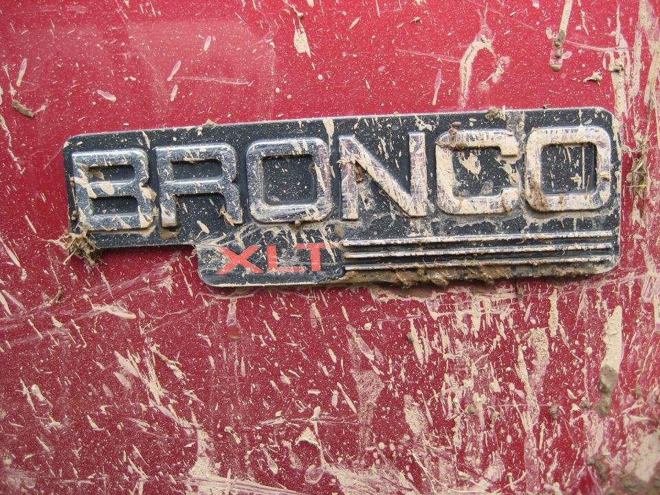 Close-up of a muddy Bronco XLT badge on a red vehicle