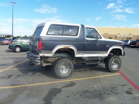 1996 Ford Bronco - Lifted blue and white Ford Bronco parked in a lot with another SUV behind it.