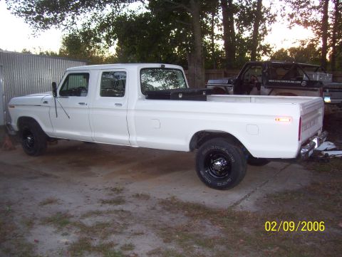1978 Ford Bronco - White late-1970s Ford crew cab long-bed pickup shot from the driver's side rear three-quarter in a gravel and grass yard, wearing black ste…