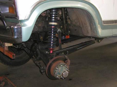 1984 Ford Bronco - Front suspension close-up on a light green and white Ford truck with the wheel removed, showing a black coilover shock with red spring perc…
