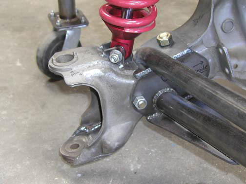 Close-up of a metal suspension part with a red coilover shock and a wheel on a stand
