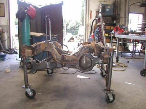 1984 Ford Bronco - A rusty solid front axle assembly with cast differential housing and welded-on radius arm mounts sits on a homemade tube dolly with swivel…