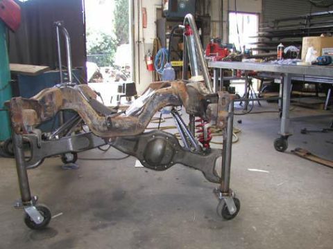 1984 Ford Bronco - A disassembled vehicle chassis sits on a wheeled stand, awaiting repair or restoration in a cluttered garage.