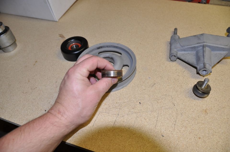Hand holding a worn bearing next to a pulley and bracket
