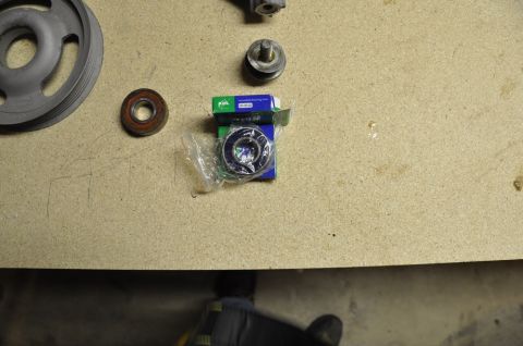 1996 Ford Bronco - A pulley and two bearings are laid out on a workbench, with one bearing still in its original packaging.