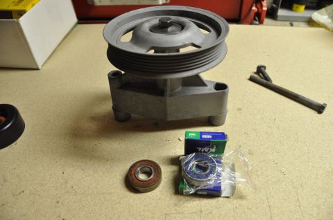 1996 Ford Bronco - A pulley assembly, two bearings, and a bolt are laid out on a workbench, likely for a vehicle repair.