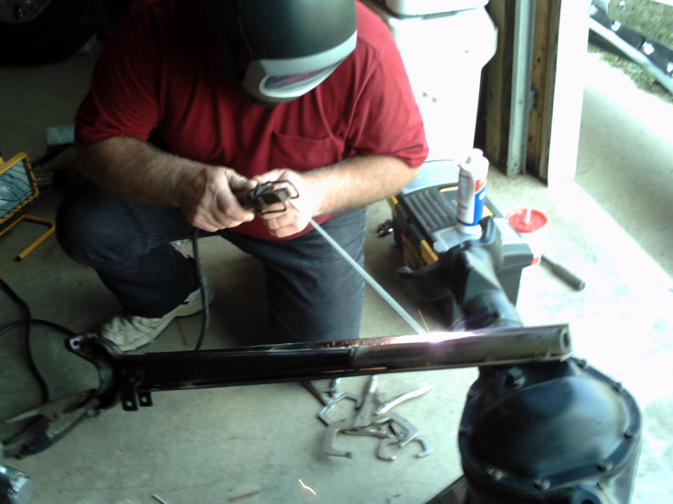 Welder in red shirt and welding mask works on a black metal frame part with sparks flying