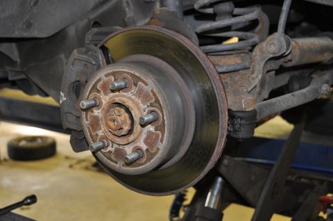 1996 Ford Bronco - Close-up view of a vehicle's rear brake rotor and suspension system, showing wear and rust.