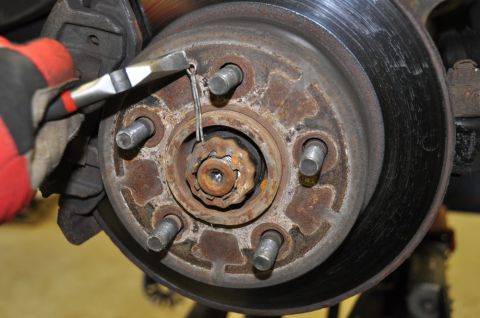 1996 Ford Bronco - A gloved hand uses pliers to remove a cotter pin from a vehicle's wheel hub assembly.