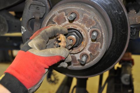 1996 Ford Bronco - A gloved hand works on a rusty wheel hub assembly, removing a cotter pin.