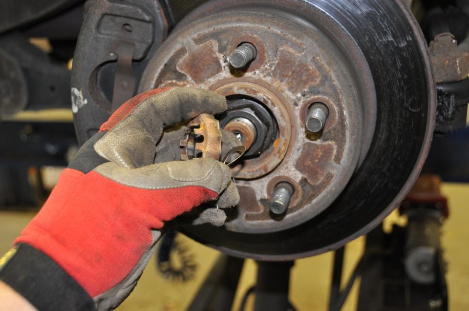Gloved hand removing a cotter pin from a rusty wheel hub assembly