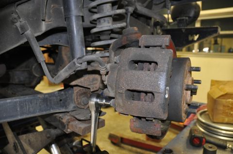 1996 Ford Bronco - A mechanic works on a vehicle's brake caliper, showing the rusty components and suspension system.