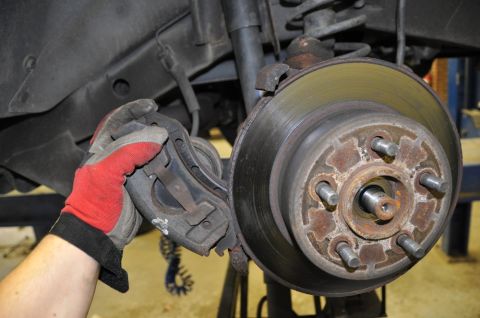 1996 Ford Bronco - Mechanic replacing brake caliper on a vehicle's wheel hub assembly.