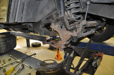 1996 Ford Bronco - Close-up of a rusty Jeep front suspension assembly undergoing repair, with tools scattered nearby.