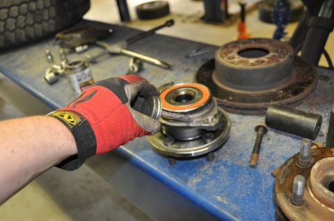 1996 Ford Bronco - A mechanic works on replacing a wheel bearing assembly, with various automotive parts laid out on a blue workbench.